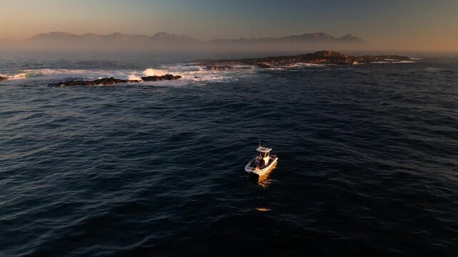 Aerial view of a lone boat on the dark ocean waters near Robben Island, with Table Mountain faintly visible in the background, Cape Town, Western Cape, South Africa.