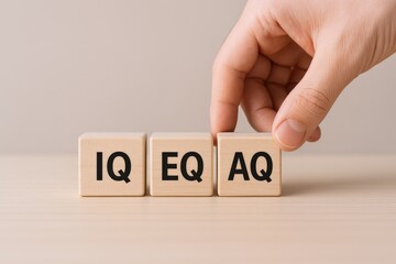 Hand Arranging Wooden Blocks Displaying IQ, EQ, and AQ for Intelligence, Emotional, and Adaptability Quotient