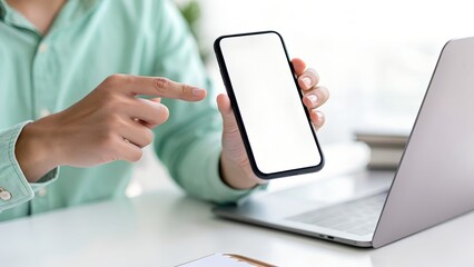 Man pointing at a smartphone with a blank screen next to a laptop on a desk, showcasing mobile technology and business applications