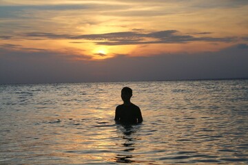 Silhouette of a man standing in the calm sea watching the sunset, ideal for travel and relaxation concepts