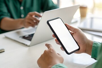 Closeup of a person holding a smartphone with a blank screen while working on a laptop, showcasing modern technology and digital communication