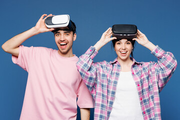 Young couple two friends family man woman they wear pink casual clothes together watching in vr headset pc gadget take off goggles isolated on plain blue background studio portrait. Lifestyle concept.