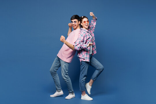 Full body young happy couple two friends family man woman wear pink casual clothes sunglasses together doing winner gesture celebrate clench fist stand back to back isolated on plain blue background.