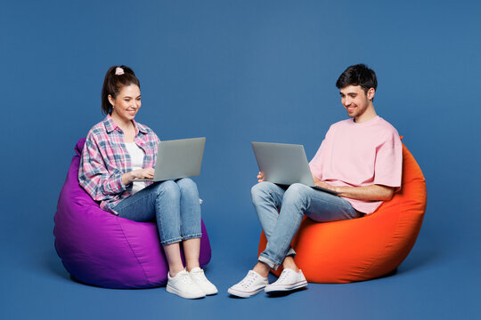 Full body young couple two friends family IT man woman they wear pink casual clothes together sit in bag chair hold use work on laptop pc computer isolated on plain blue background. Lifestyle concept. - Powered by Adobe