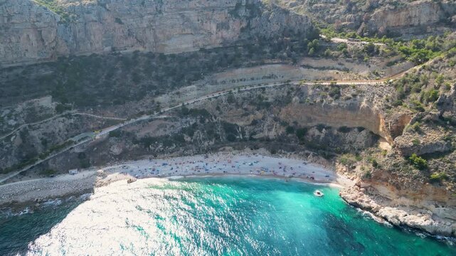 Aerial view of the vibrant Cala del Moraig beach nestled between rocky cliffs and turquoise water, a scene of serene beauty, Benitachell, Spain.