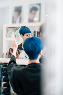 A person with vibrant blue hair holds a mirror, admiring their reflection and new hairstyle in a modern hair salon. They are checking their fresh look.