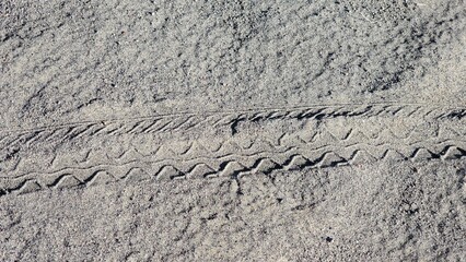 Zigzag tire track pattern on light sandy ground, outdoor texture background