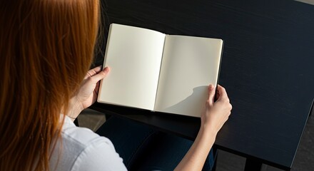Woman with red hair holds an open blank notebook seated at a dark table