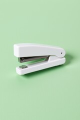 White stapler with silver metal accents rests on a textured light green background