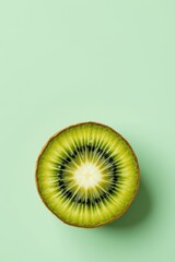 Close up of a sliced kiwi fruit showing vibrant green flesh and black seeds on a light green background
