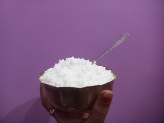 This image shows a metal bowl filled with white sago pearls (sabudana) placed inside a larger brass plate.A spoon rests inside the bowl, scooping some of the sago pearls.