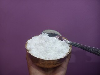 This image shows a metal bowl filled with white sago pearls (sabudana) placed inside a larger brass plate.A spoon rests inside the bowl, scooping some of the sago pearls.