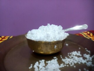 This image shows a metal bowl filled with white sago pearls (sabudana) placed inside a larger brass plate.A spoon rests inside the bowl, scooping some of the sago pearls.