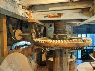 Interior and mechanism of an old wooden mill of the 18th century. Wooden gears and main shaft grinding grain genuine obsolete technologies of the past. Natural light.