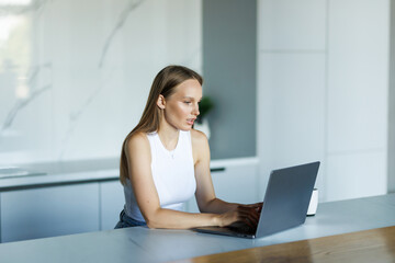 Fototapeta premium Young woman is sitting at the kitchen table with laptop