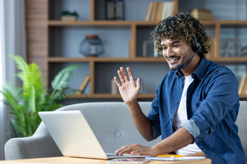 A cheerful individual participates in an online meeting while sitting on a couch and waving....