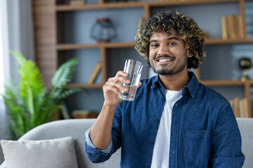 A cheerful person enjoys a refreshing glass of water while seated in a home environment with modern decor.