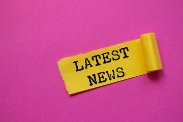 Latest news message written on ripped torn yellow paper piece on pink background. Conceptual latest news symbol. Copy space.
