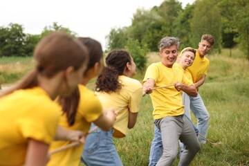 Fototapeta premium Team building. Group of happy people playing tug of war with rope outdoors