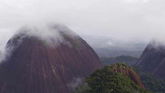 Aerial view of the majestic Cerros de Mavicure mountains veiled in mist, their dark rock contrasting with the vibrant green canopy, Cerros Mavicure, Colombia.