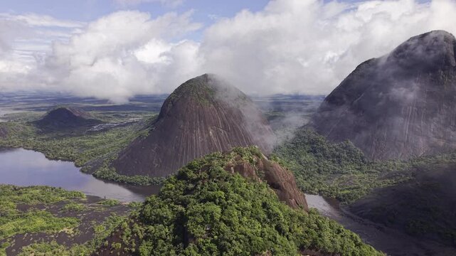 Aerial view of the Cerros Mavicure peaks rising majestically amidst the lush Amazon rainforest, with clouds clinging to their summits, Cerros Mavicure, Colombia.