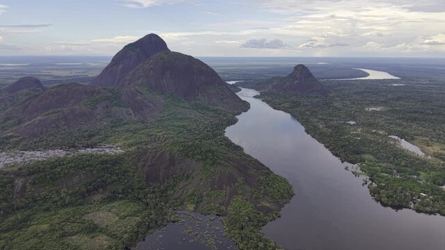 Aerial view of Cerros de Mavicure, where the dark river winds through lush green rainforest and around the imposing rock formations, Cerros Mavicure, Colombia.