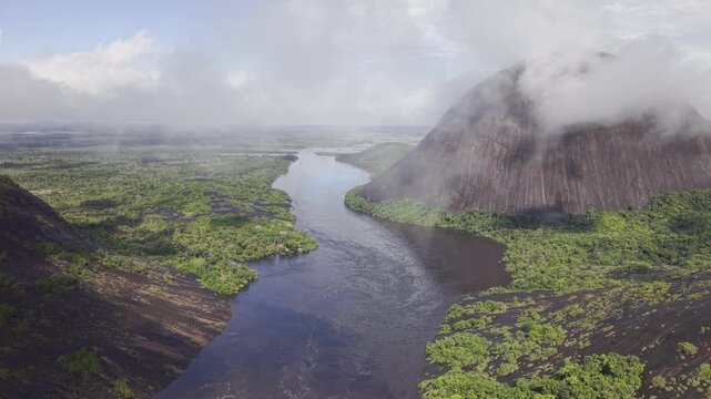 Aerial view of the dark waters of the river flowing between the rocky Cerros de Mavicure and the lush green forest, Cerros Mavicure, Colombia.