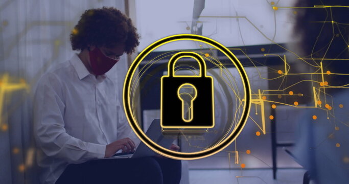 Showing golden padlock overlay in modern office with masked worker and colleague typing on laptops - Powered by Adobe