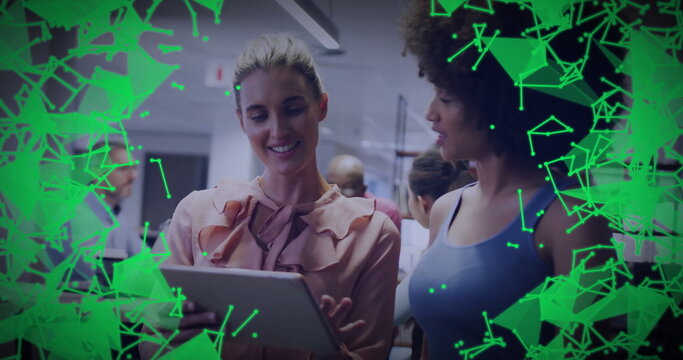 Female colleagues in workwear reviewing tablet in office, showing abstract green network overlay