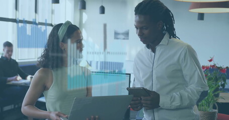 Collaborating woman in green top and man in white shirt using laptop and tablet in office