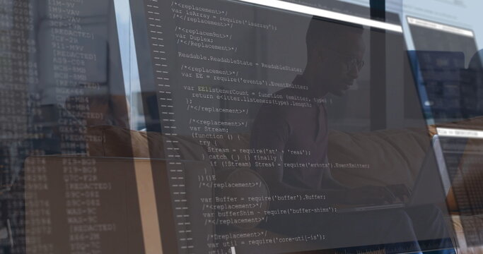 Developer wearing shirt and glasses typing code in office, with 3 screens showing JavaScript code