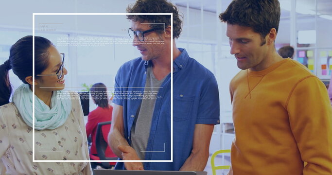 Collaborating colleagues reviewing project on open-plan office desk, with laptop, sticky note board