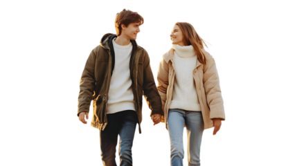 A young couple holding hands and walking together wearing winter coats and jeans looking at each other
