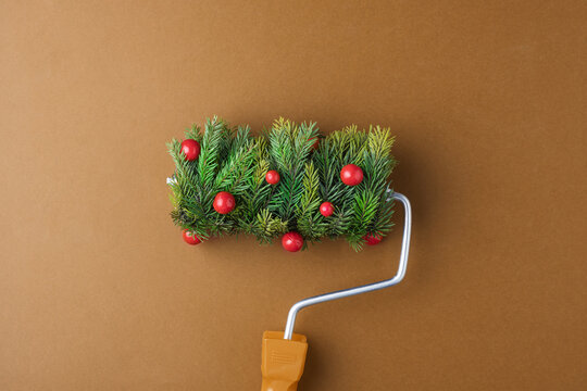 Festive paint roller with fir sprigs and red berries on warm brown backdrop promises cozy holiday makeover and playful Christmas mood.