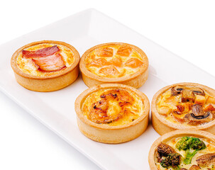 Assorted savory tarts with fillings served on a white platter
