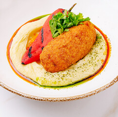 Delicious dish featuring crispy croquette on smooth hummus with peppers