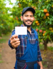 Farm Hand with a Blank Card: A smiling farm worker, radiating warmth, extends a pristine blank card toward the viewer, inviting an open exchange amidst the bounty of an orchard.