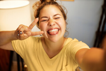 Closeup of cute funny ,millennial female in home clothes grimacing making faces and showing v-sign...