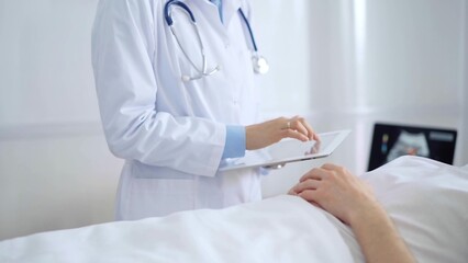 Doctor consulting patient with digital tablet in hospital room. Healthcare professional providing care