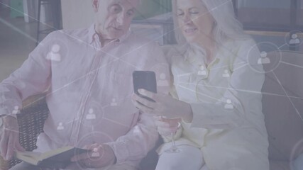 Senior couple sitting, woman turning phone toward man, social network icons growing showing links - Powered by Adobe