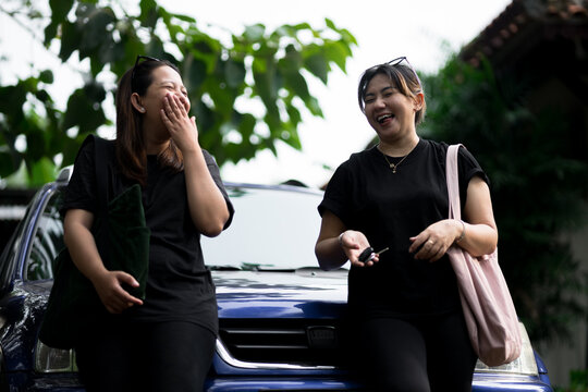 Two women in black shirts engaged in conversation, smiling, with a blurred nature background, captured in candid style.