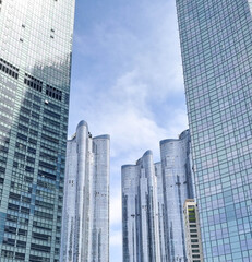 Obraz premium A group of modern skyscrapers with glass facades reaching towards a blue sky with scattered clouds, creating an urban architectural landscape