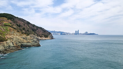 
 Rocky coastline with cliffs and sparse vegetation, turquoise sea with small waves crashing...