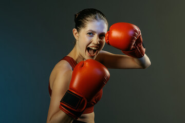Smiling female boxer in red gloves shouting pose on dark studio background