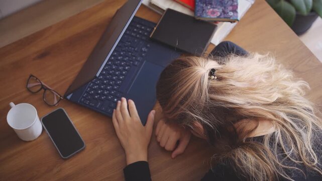 unhappy tired woman sleeping on job laptop, head lying down on desk working late overtime. office cabinet room. Sad adult blonde girl suffers from head ache top view, depression emotional burnout 4k