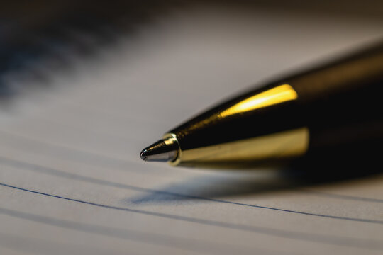 A close-up shot of the tip of a black pen resting on lined paper.