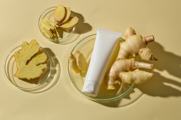 A skincare tube placed beside bowls of ginger roots and slices, photographed from above with soft beige lighting. Mockup for design