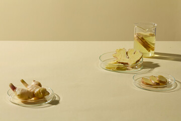 A minimalist still life of ginger slices and a small glass cup with liquid, set against a beige background. Empty space for design and add