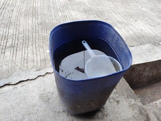 A light blue dipper in a blue bucket filled with rainwater on the terrace floor of the house