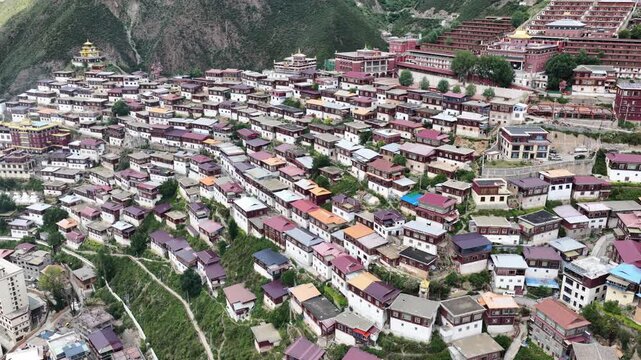 Aerial view of the Larung Gar Buddhist Institute, a vibrant tapestry of red-roofed dwellings nestled amidst the green mountains, Garz&ecirc;, Sichuan, China.